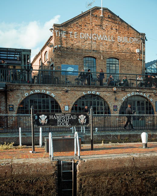 A brick building named 'The Tedingwall Building' with large arched windows on the upper and lower levels, situated along the Camden Lock area in West Hampstead. The ground level features a black metal